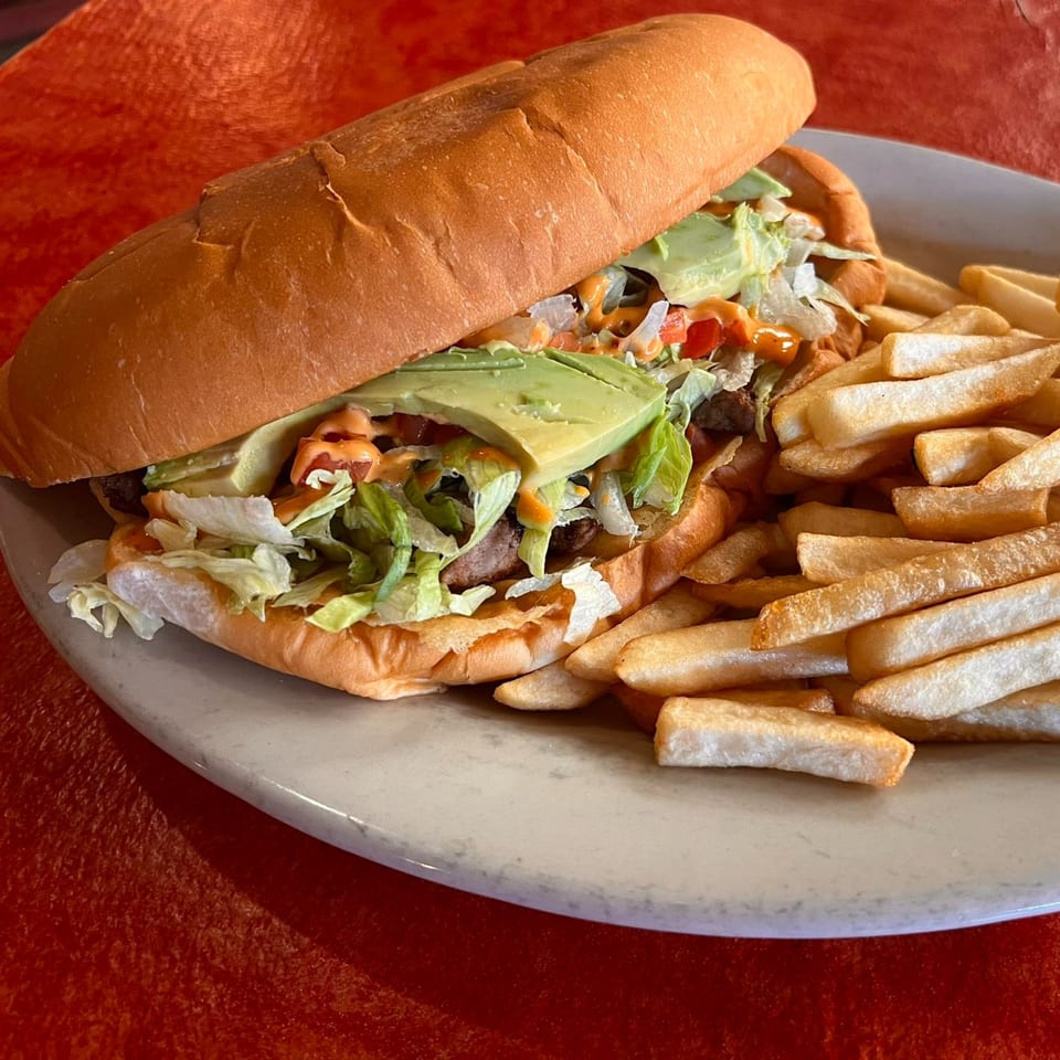 A Mexican torta sandwich with avocado, lettuce, and sauce, served with a side of french fries.