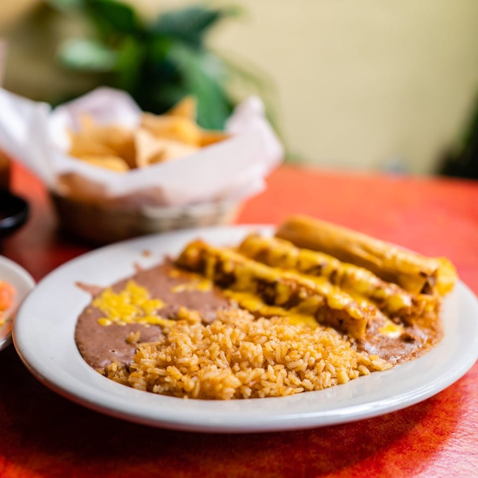 Maria's Mexican Restaurant's enchiladas with rice and refried beans, with a basket of chips in the background.