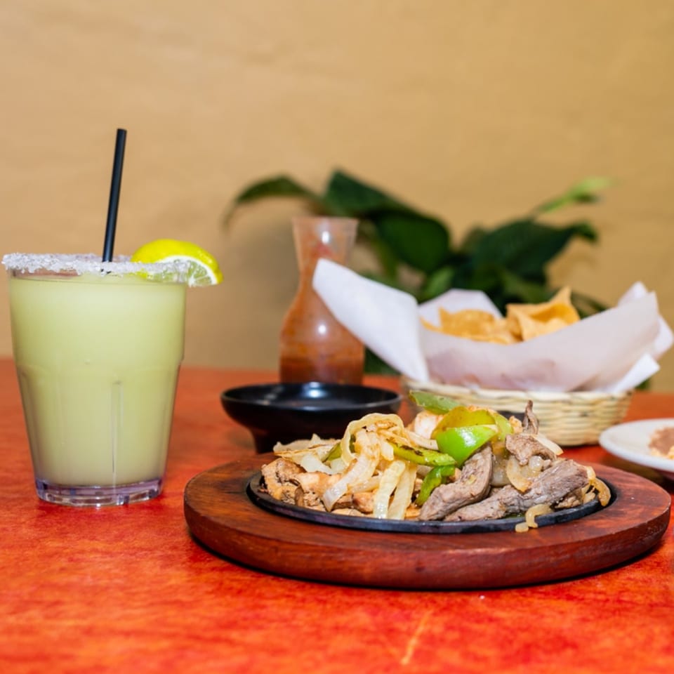 Maria's Mexican Restaurant's sizzling fajitas with a margarita, chips, and salsa on a red table.