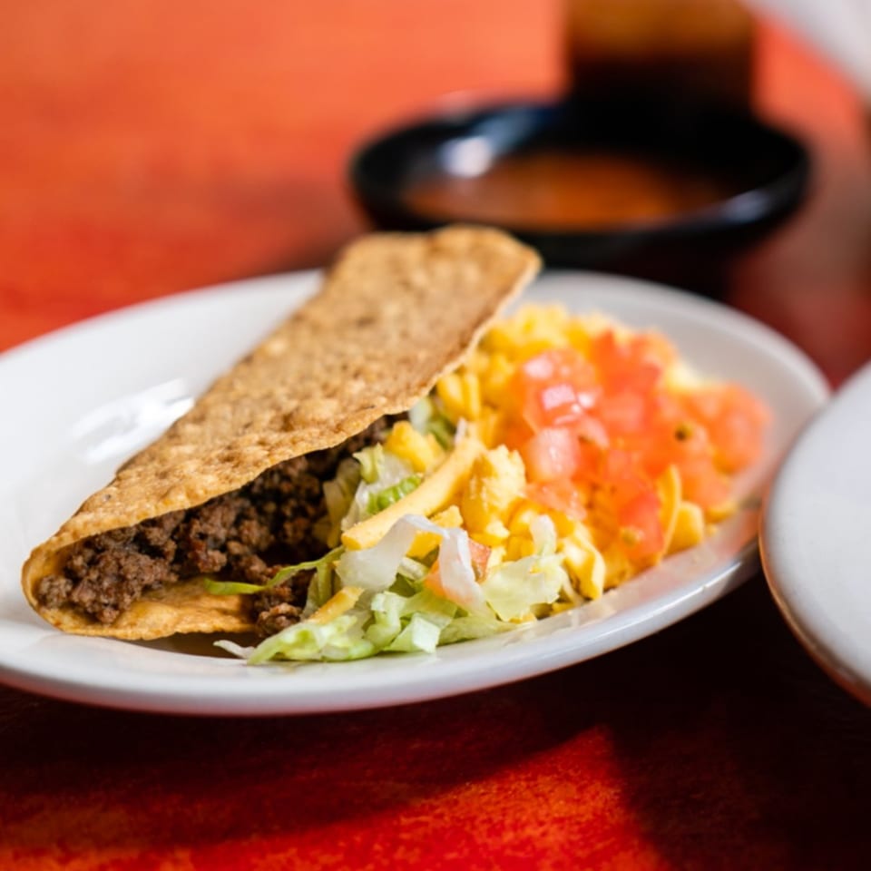 A crispy Maria's Mexican Restaurant taco filled with ground beef, lettuce, cheese, and diced tomatoes.