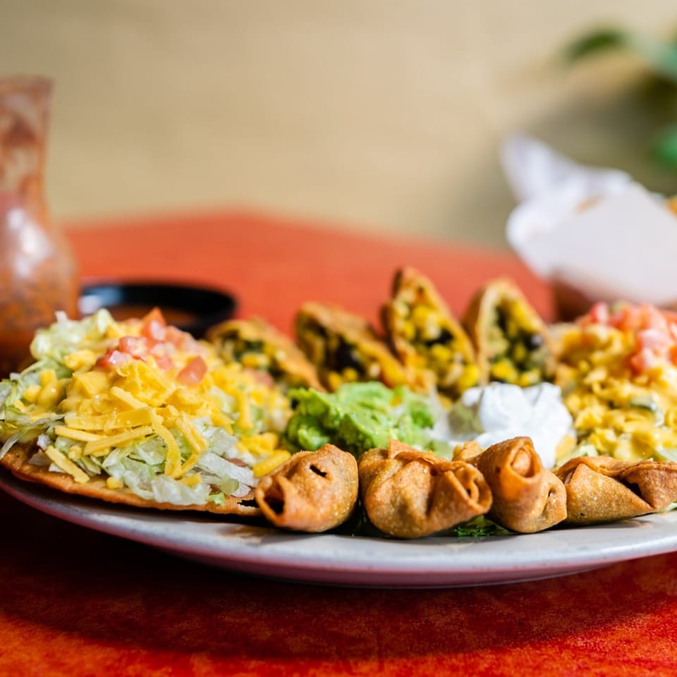 A plate of Maria's Mexican Restaurant appetizers, including tacos, taquitos, guacamole, and sour cream.