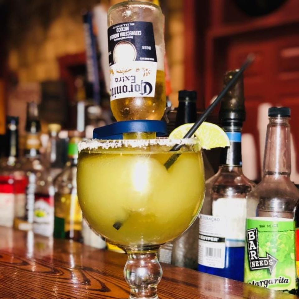 A large margarita with a Corona beer bottle inverted into it, garnished with a lime slice.
